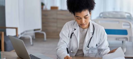 Black woman, laptop and doctor writing in notebook for healthcare test, study or research at the hospital. African American female medical expert taking notes in book for insurance, report or results.